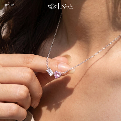 Dainty Toi et Moi necklace featuring a pastel pink heart gem paired with a clear emerald-cut cubic zirconia stone on a fine silver chain.