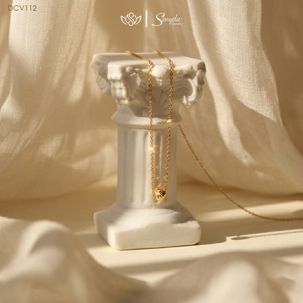 Dainty gold necklace with a single diamond-cut faceted bead floating on a fine chain resting on soft fabric.