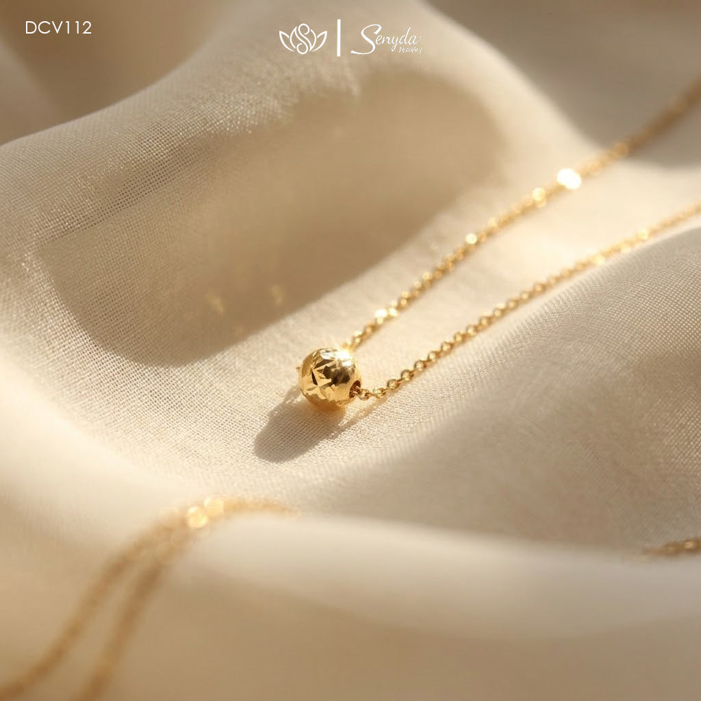 Dainty gold necklace with a single diamond-cut faceted bead floating on a fine chain resting on soft fabric.