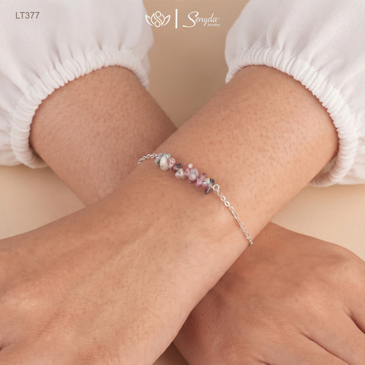 Woman wearing a dainty sterling silver bracelet with a bar of pink, green and gray tourmaline chips on her wrist