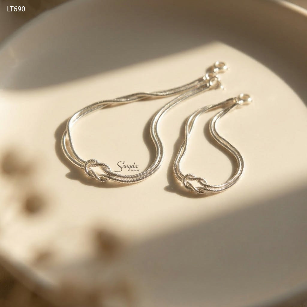 Close-up of two matching sterling silver love knot bracelets on 1.2mm snake chain, catching the light