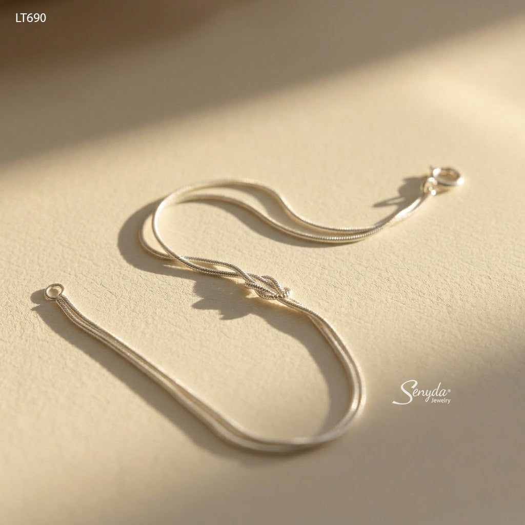 Sterling silver double snake chain bracelet tied in a love knot, shown flat on a cream background