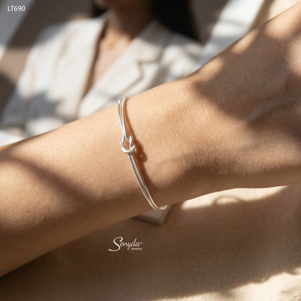 Woman wearing a dainty sterling silver love knot bracelet made of two 1.2mm snake chains