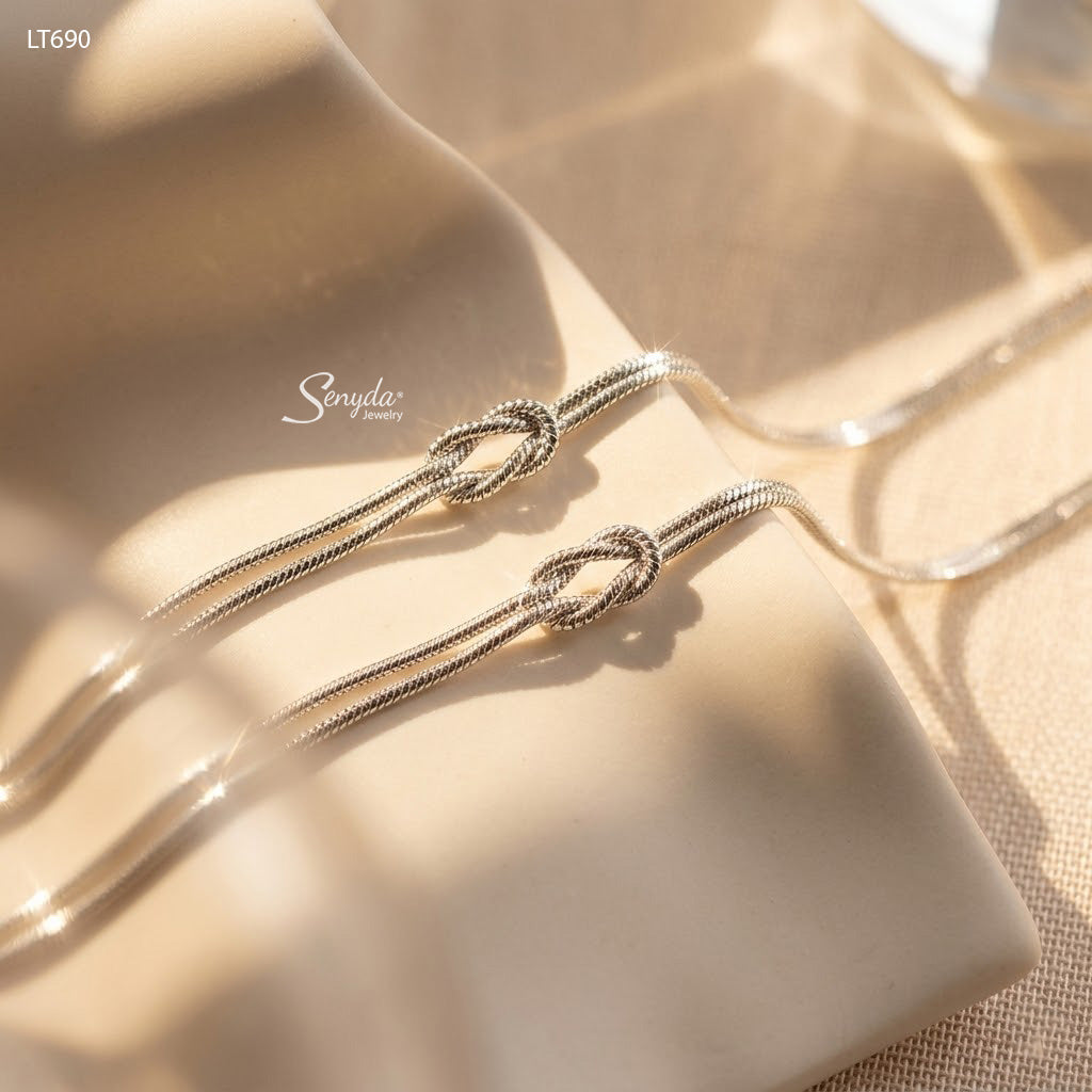 Close-up of two matching sterling silver love knot bracelets on 1.2mm snake chain, catching the light