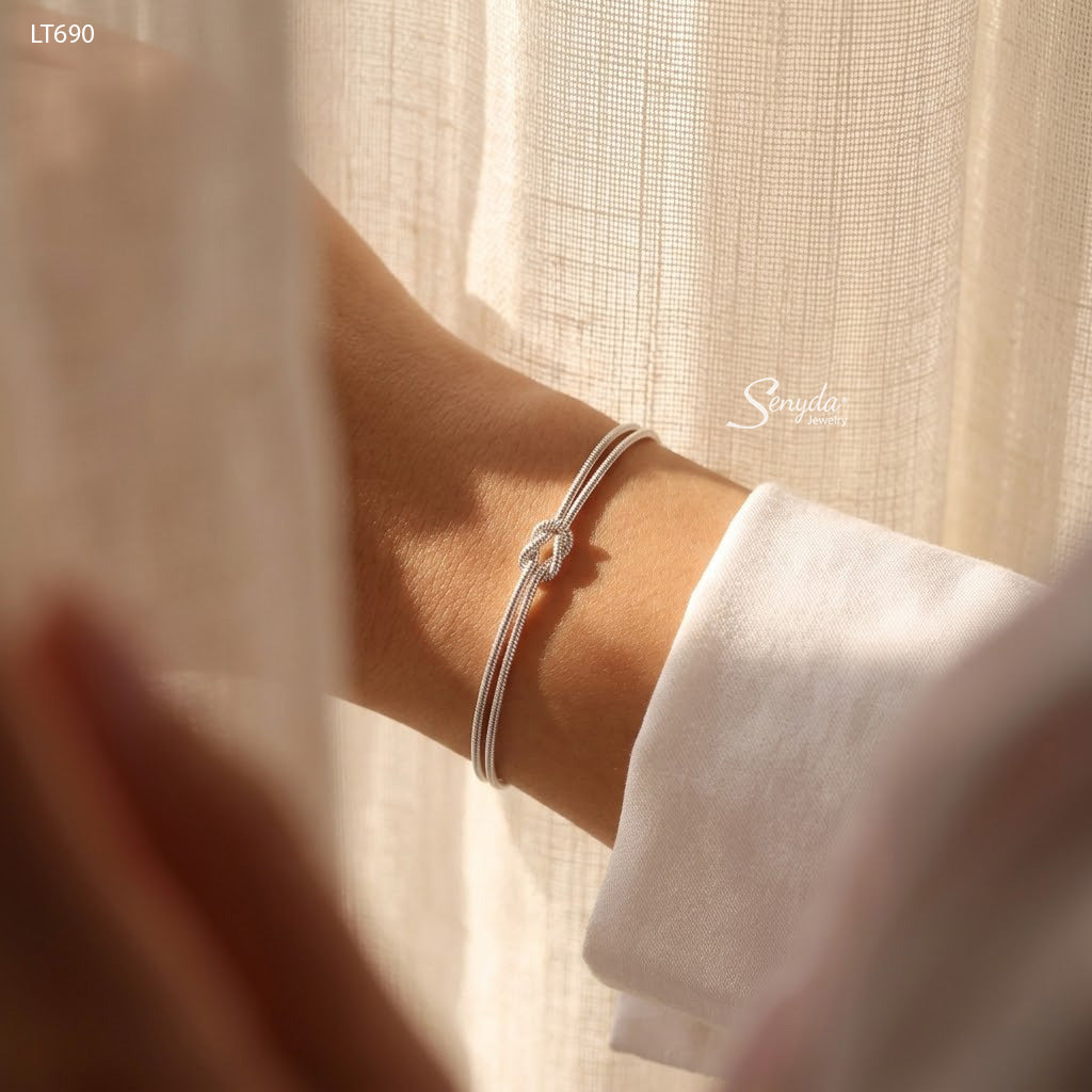 Woman wearing a dainty sterling silver love knot bracelet made of two 1.2mm snake chains