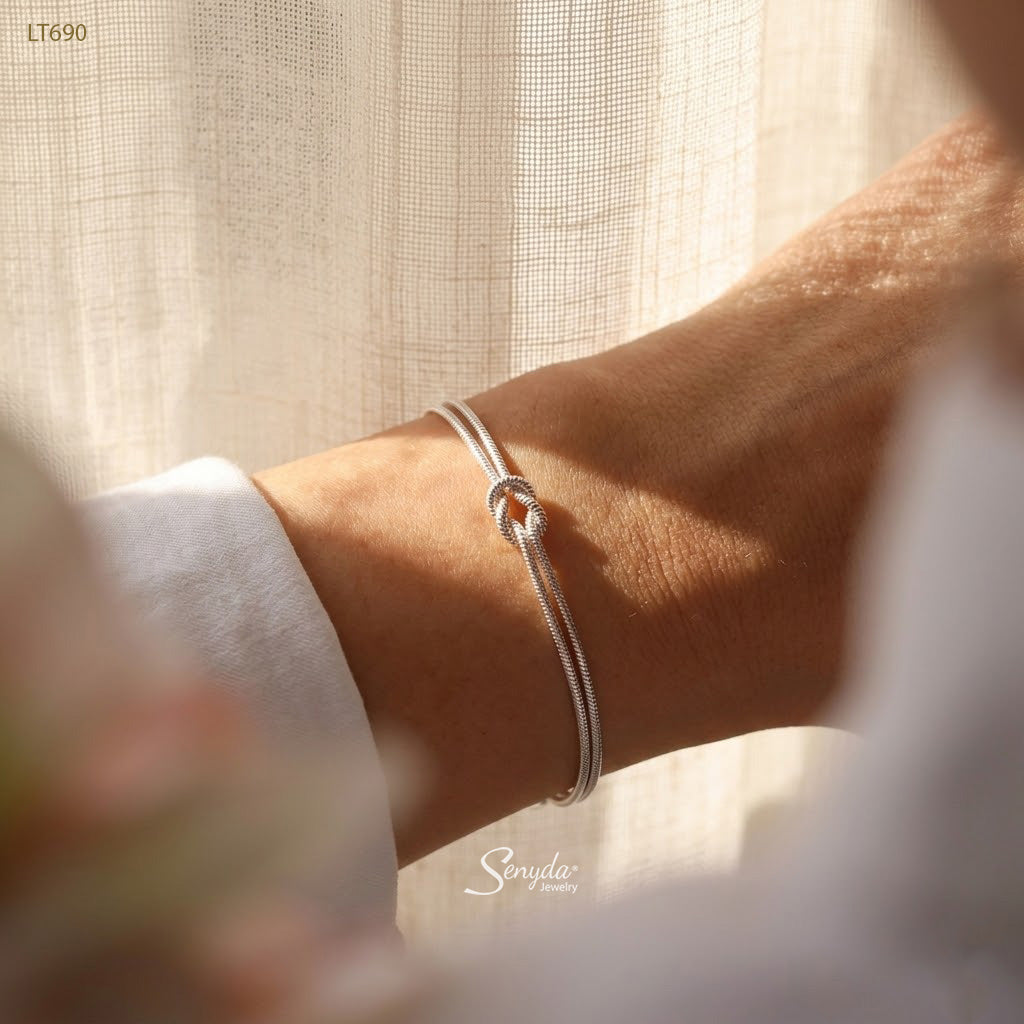 Woman wearing a dainty sterling silver love knot bracelet made of two 1.2mm snake chains
