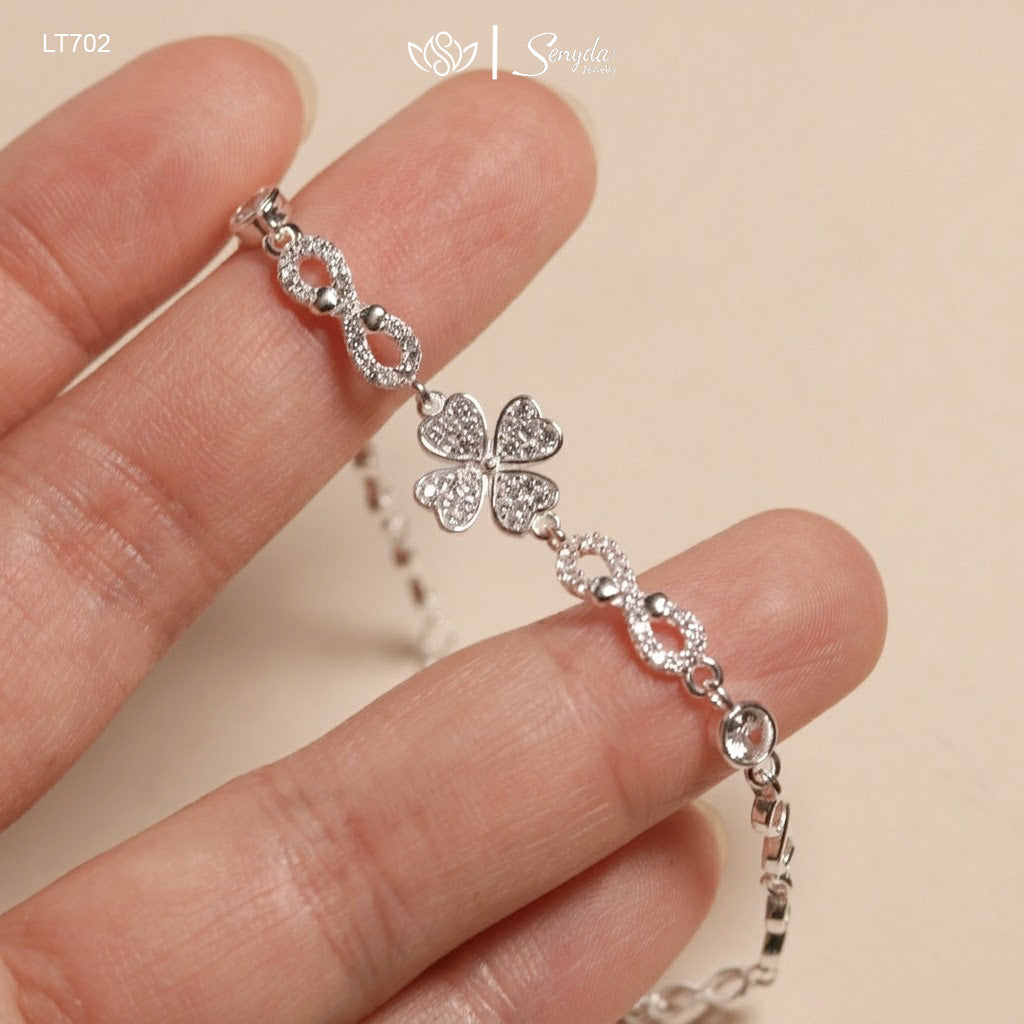 Close-up of a pavé CZ four leaf clover with heart-shaped leaves between two sparkling infinity links, held in fingers