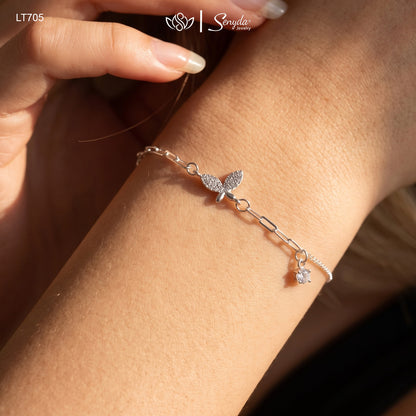 Woman wearing a sterling silver paperclip chain bracelet with a pavé cubic zirconia butterfly and a solitaire CZ charm