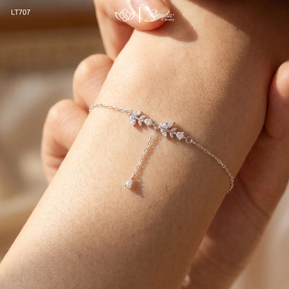 Woman wearing a dainty silver leaf branch bracelet with sparkling cubic zirconia and a teardrop drop on her wrist