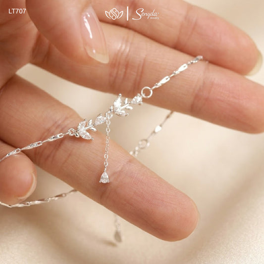 Hand holding a sterling silver leaf branch bracelet with marquise cubic zirconia leaves and a teardrop CZ dangle