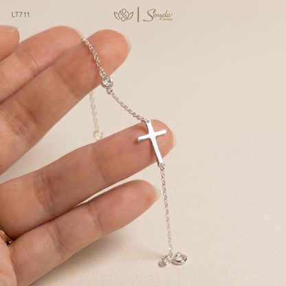 A silver lariat-style cross necklace with a small cross pendant and a clear rhinestone, held by a hand against a light beige background. The brand logo 'Sonya jewelry' is visible at the top.