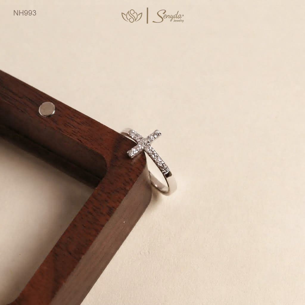 Silver cross ring with pavé CZ stones resting on the edge of a walnut wood jewelry tray