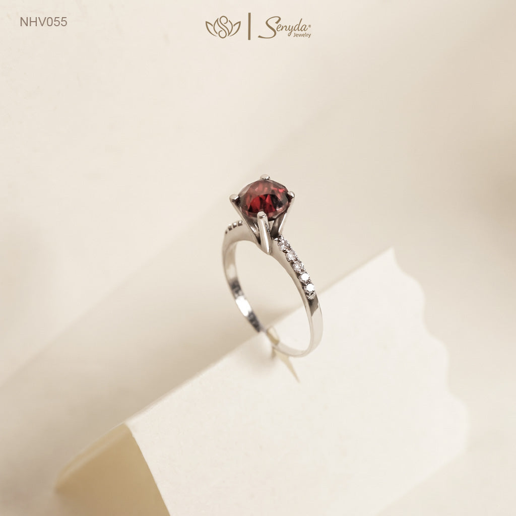 Solid white gold ring with a round deep red garnet in a four-prong setting and a row of pavé side stones on the band