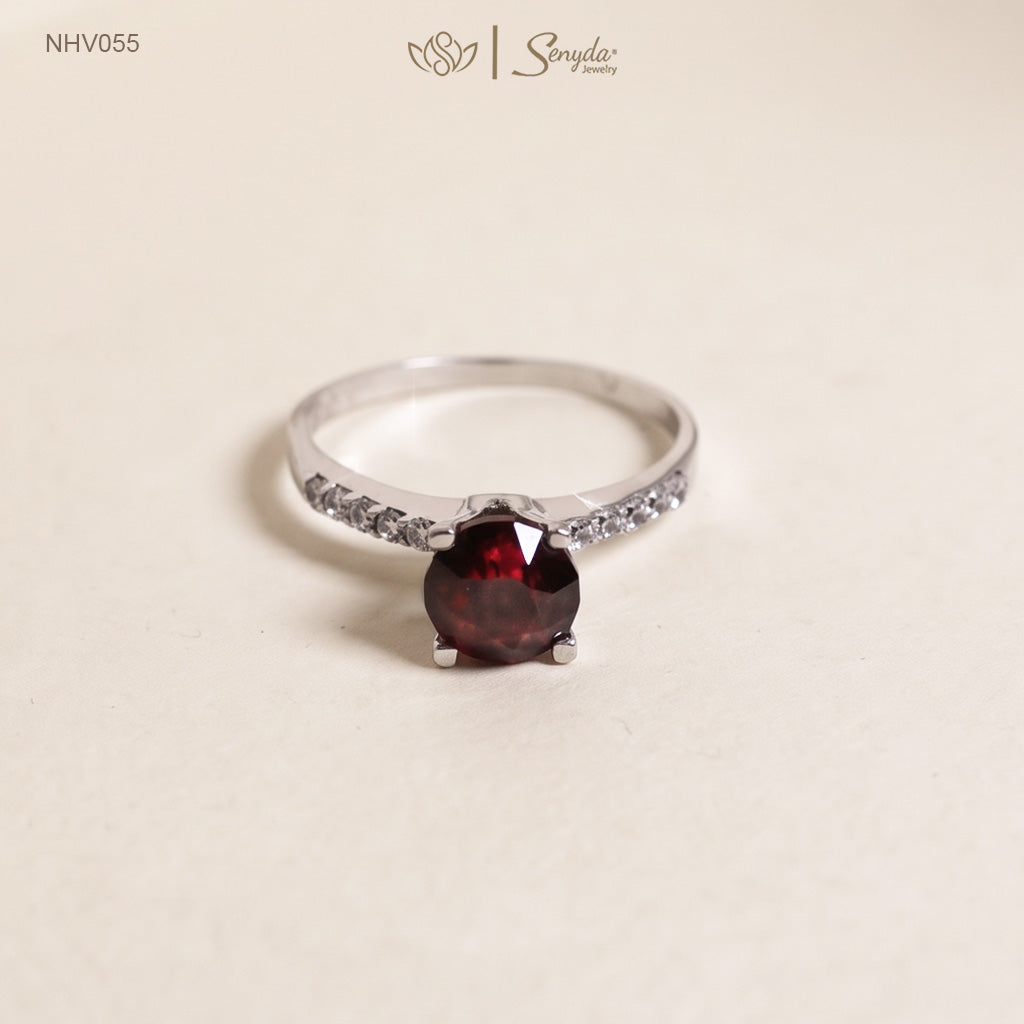 Solid white gold ring with a round deep red garnet in a four-prong setting and a row of pavé side stones on the band