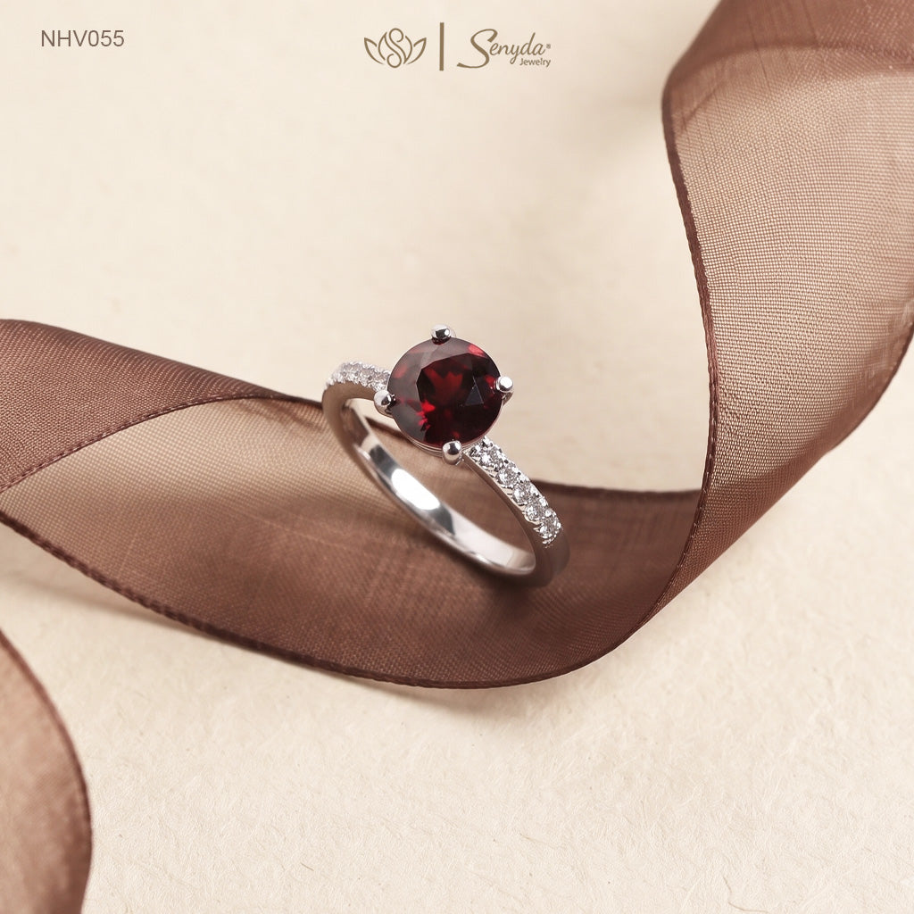 Solid white gold ring with a round deep red garnet in a four-prong setting and a row of pavé side stones on the band