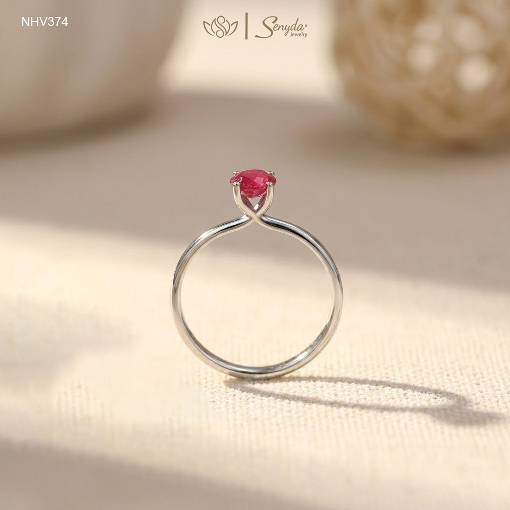 Dainty solid gold solitaire ring with a round red ruby in a four-prong setting on a cream background.