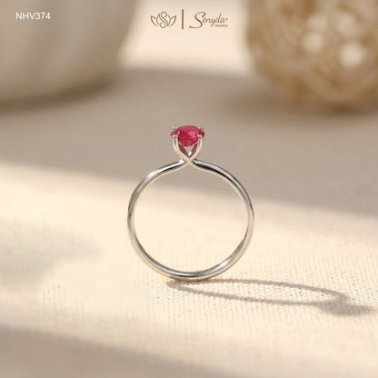 Dainty solid gold solitaire ring with a round red ruby in a four-prong setting on a cream background.