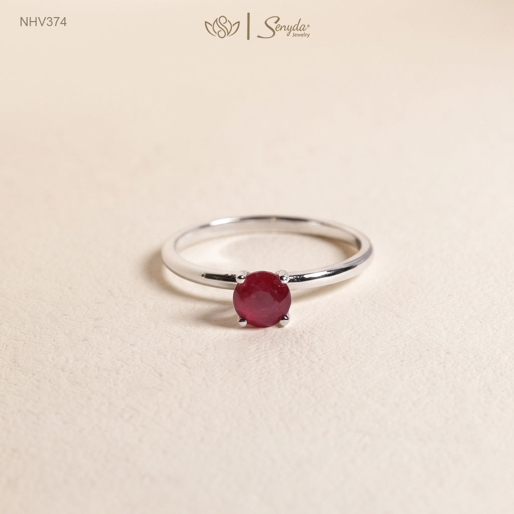 Dainty solid gold solitaire ring with a round red ruby in a four-prong setting on a cream background.