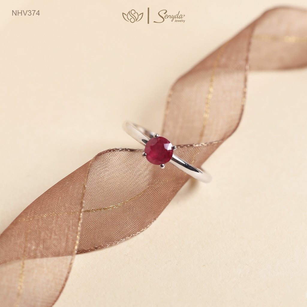 Dainty solid gold solitaire ring with a round red ruby in a four-prong setting on a cream background.