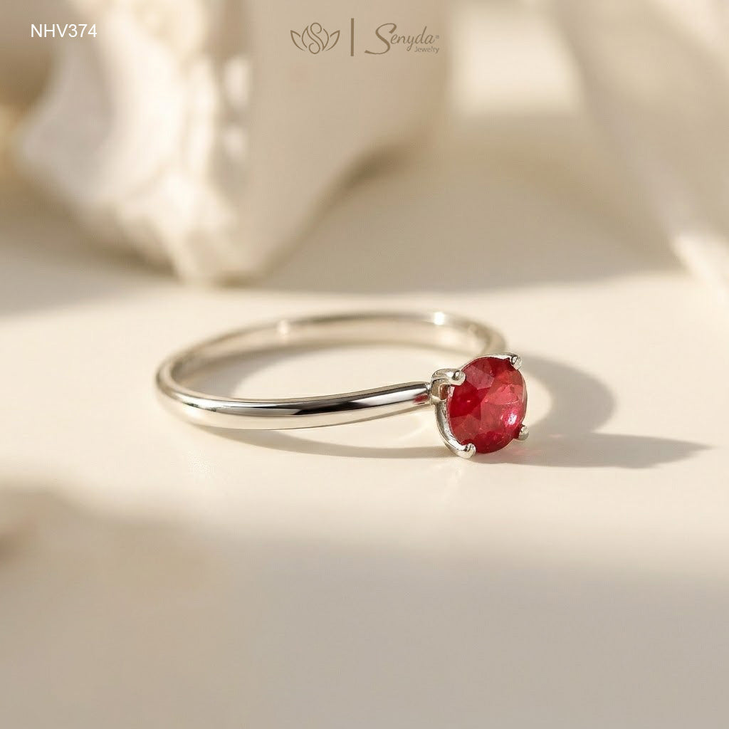 Dainty solid gold solitaire ring with a round red ruby in a four-prong setting on a cream background.